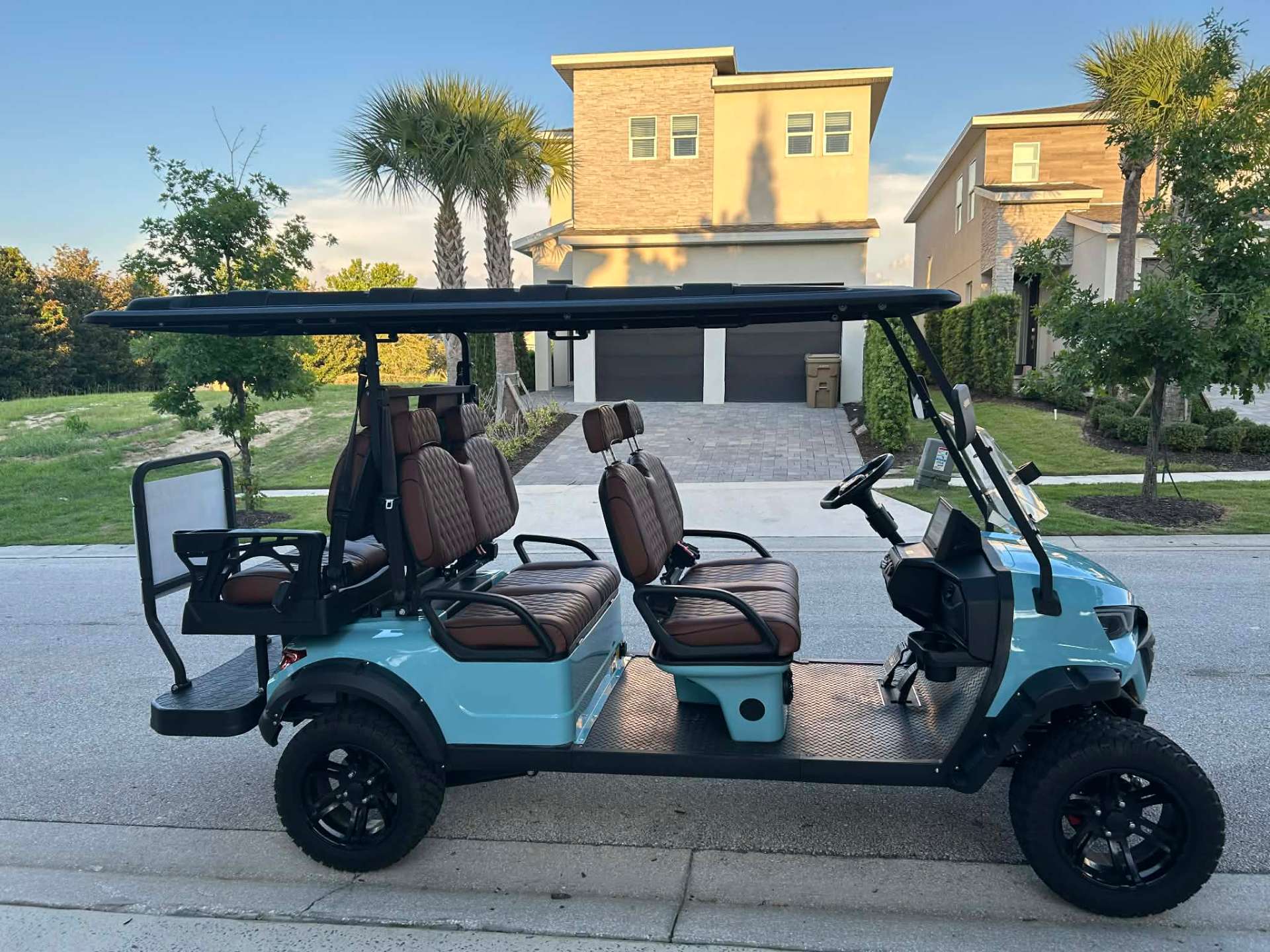 Side view of teal 6-seater lifted golf cart parked at a Reunion Resort vacation home at golden hour
